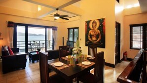 Un coin repas avec une table dressée pour quatre personnes, un tableau représentant un Bouddha accroché au mur et une vue sur la mer par de grandes fenêtres.