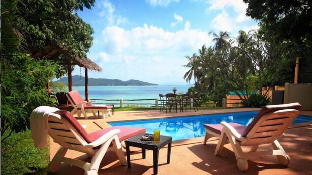 Un espace aménagé au bord de la piscine, avec des chaises longues et une table, d’où l’on peut admirer une mer d’un bleu limpide et des îles lointaines.