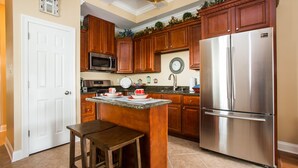A kitchen with wooden cabinets, a stainless steel refrigerator, a microwave, and a dining area with stools. - TOP LOCATION! Luxury Traditional New Orleans Home, Heart of NOLA (New Orleans)