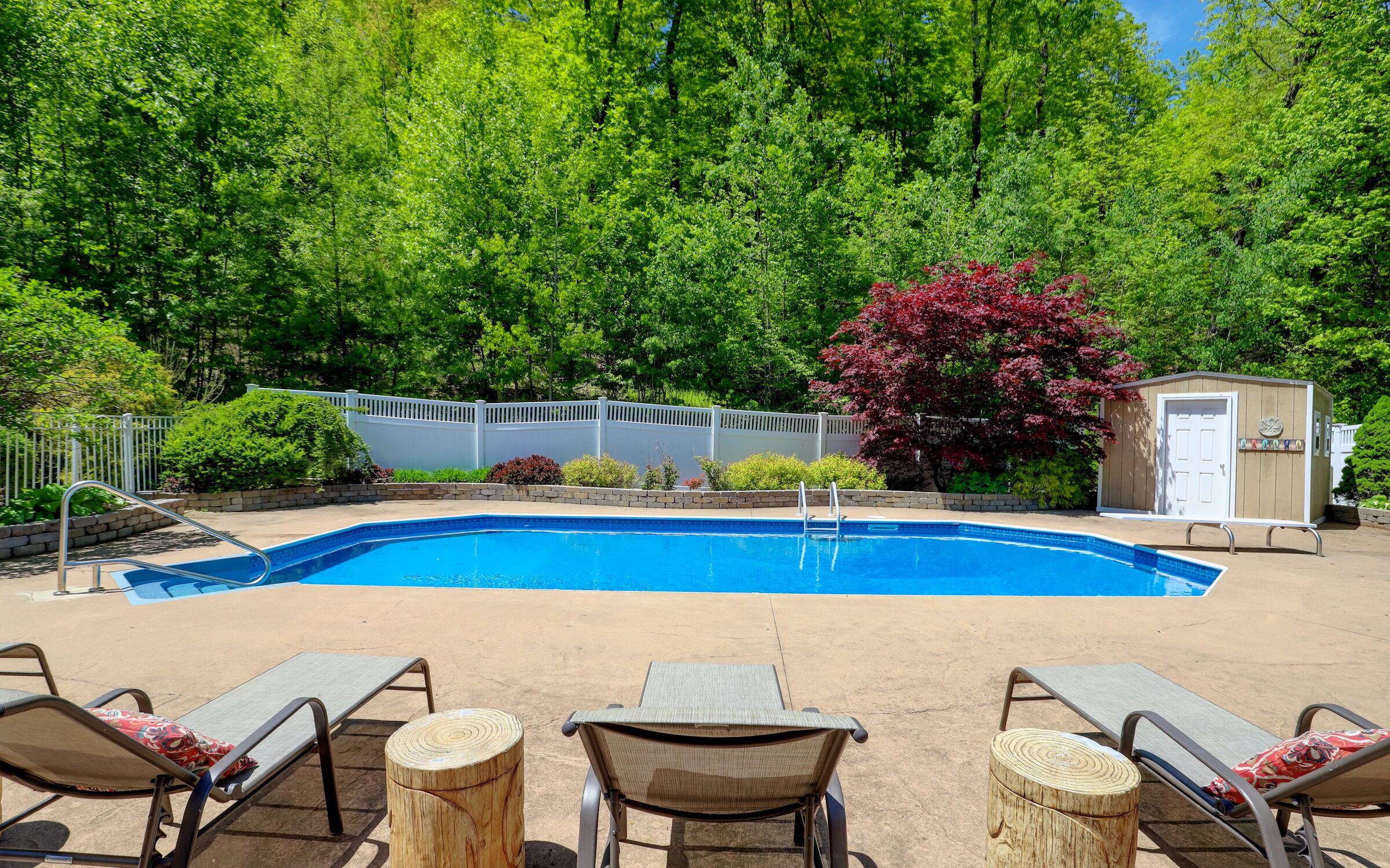 A backyard with a swimming pool, lounge chairs, and a wooden shed.