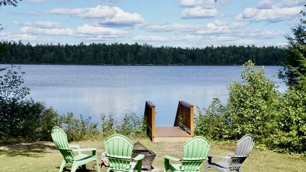 A lakeside deck with four green Adirondack chairs and a wooden bench. - Your Maine Lake Escape — Waterfront, Peaceful, Pet-Friendly (Sullivan)