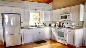 A kitchen with white cabinets, a stainless steel refrigerator, a microwave, a stove, and a sink. - Your Maine Lake Escape — Waterfront, Peaceful, Pet-Friendly (Sullivan)