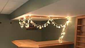 A wooden bar area with three stools, string lights, and a poster on the wall. - Family Cottage Close to Beach!! (Harwichport)