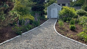 A gravel path leading to a small shed surrounded by lush greenery and flowering plants. - Family Cottage Close to Beach!! (Harwichport)