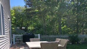 A wooden deck with a picnic table and wicker chairs, surrounded by a white picket fence and greenery. - Family Cottage Close to Beach!! (Harwichport)