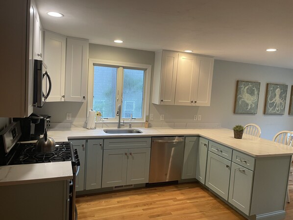 A modern kitchen with white cabinets, stainless steel appliances, a large window, and artwork on the wall.