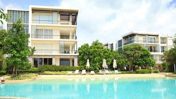 A modern multi-story hotel with a swimming pool, lounge chairs, and greenery. - Baan Nub Kluen Condo - Hua Hin (Tambon Nong Kae)