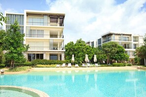 Un hôtel moderne à plusieurs étages, doté d’une piscine, de chaises longues et d’un espace verdoyant.