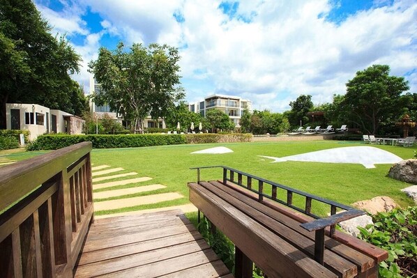Un parc doté d’une terrasse en bois, d’une pelouse agrémentée d’un motif géométrique blanc, et d’un bâtiment visible au loin.
