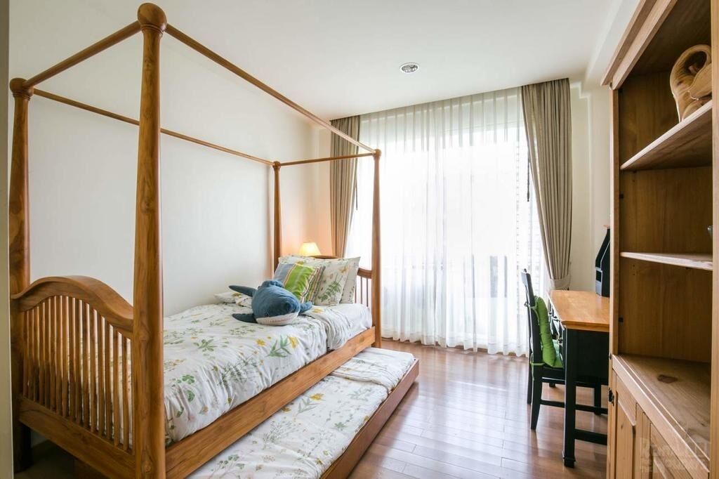 A four-poster bed with a wooden frame, a bench at the foot, and a wooden desk with a chair.