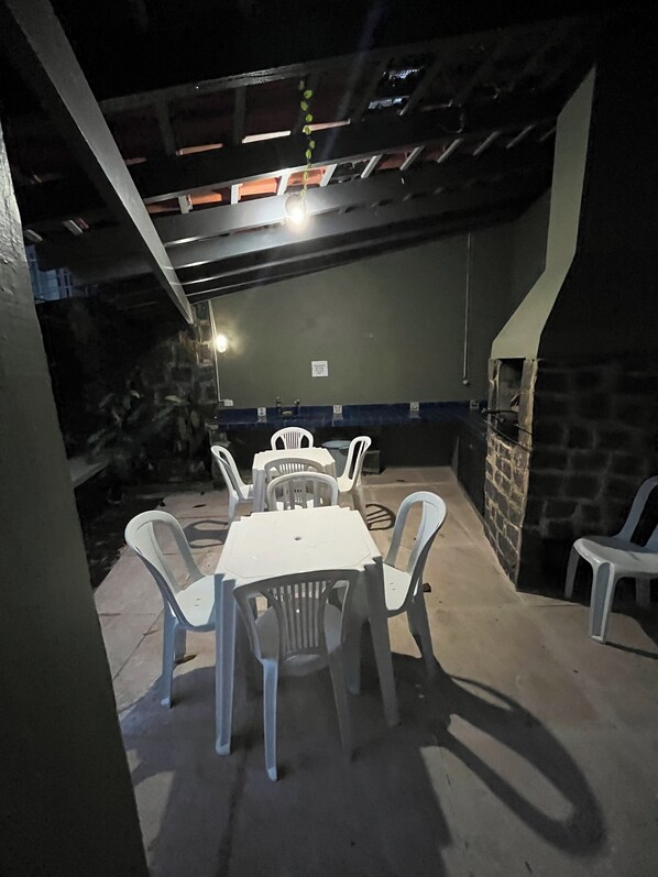 An outdoor patio with a table and chairs, a stone wall, and a chimney. - Almost on the sand, Cond. Closed, Air Cond, 4 suites, 12 guests. 8 adults and 4 children (Ubatuba)