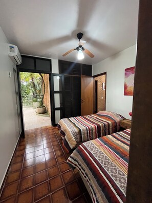 A room with two beds, a ceiling fan, and a view of a garden through an open door. - Domingas Dias, 80m from the sea, 4 suites with pool. (Ubatuba)