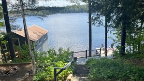 A wooden staircase leading to a dock by a lake, surrounded by trees and a cabin. - Picturesque Adirondack Lake Home (Greig)