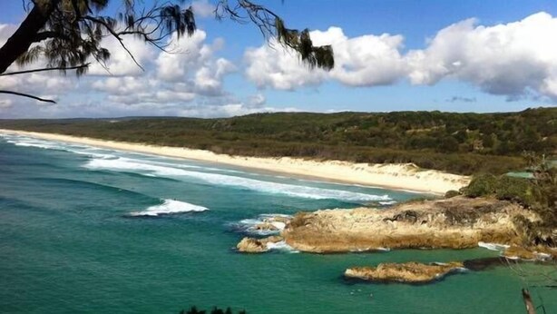 Un paisaje costero con aguas turquesas cristalinas, una playa arenosa y afloramientos rocosos.