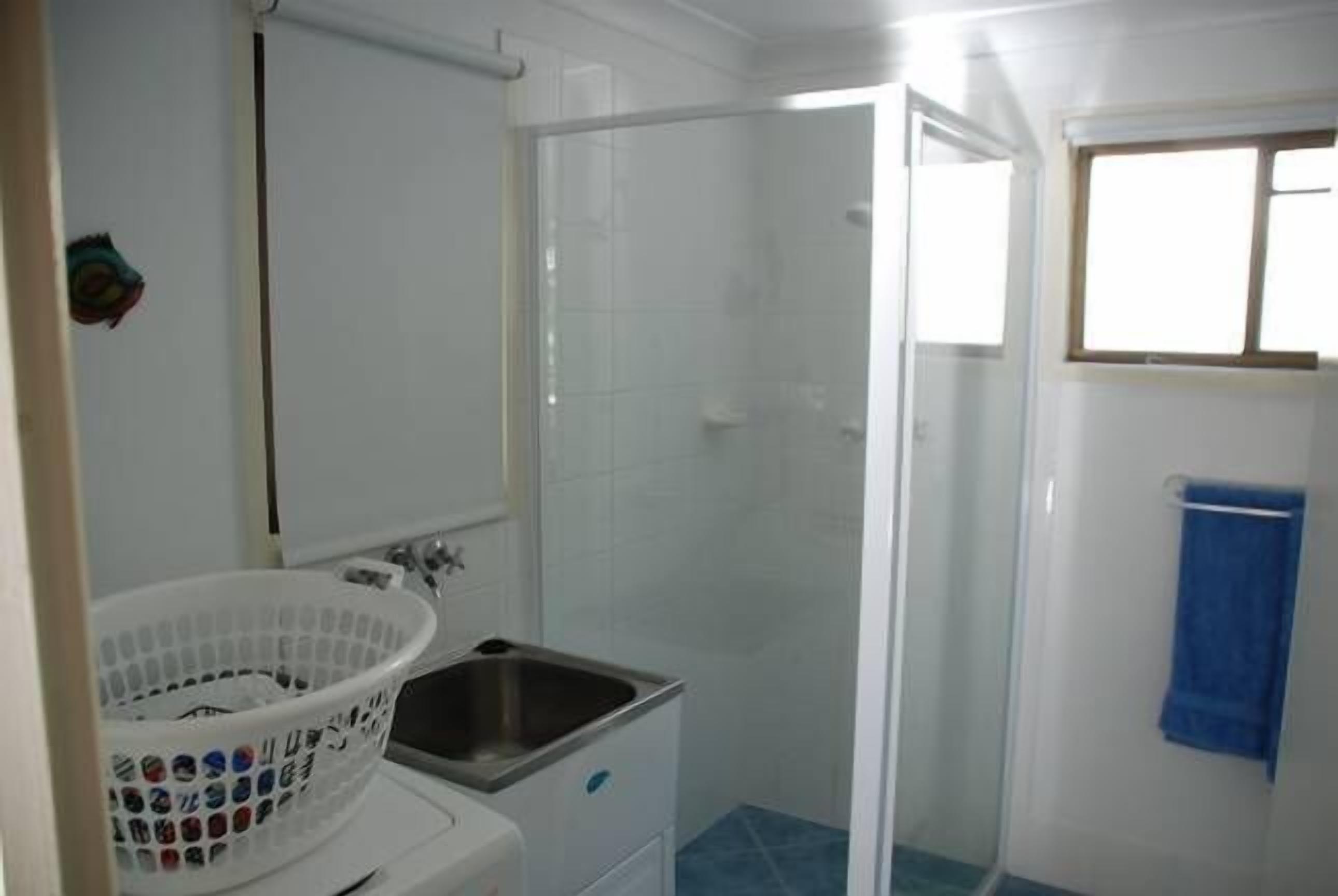 A bathroom with a shower, a sink, and a white laundry basket.