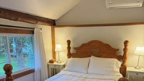 A wooden four-poster bed with white bedding, two bedside lamps, and an air conditioning unit on the wall. - Cooperstown Area Charming Carriage House (Mount Vision)