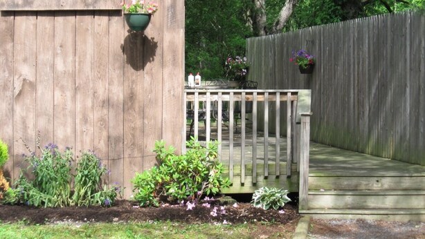 A wooden deck with a white railing, surrounded by a wooden fence and various plants. - Cooperstown Area Charming Carriage House (Mount Vision)
