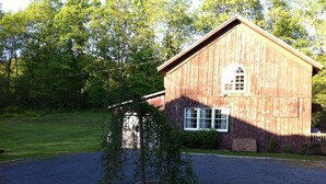A wooden barn with a large window and a gravel driveway. - Cooperstown Area Charming Carriage House (Mount Vision)