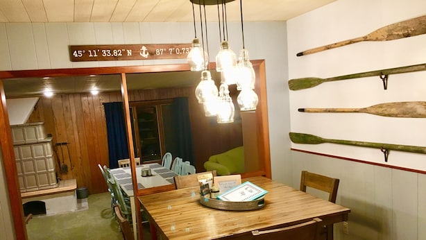 Een eetgedeelte met een houten tafel en stoelen, een hanglamp en een wand met houten planken.