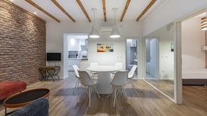 Un salon moderne comprenant un coin repas, des poutres en bois, un mur en briques et un grand tableau.