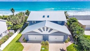A two-story house with a garage, surrounded by a well-maintained lawn and palm trees, overlooking a beach.
