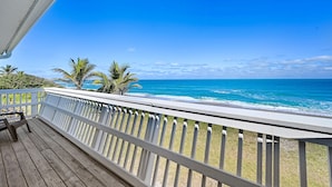 A wooden deck with a white railing overlooking a beach with palm trees and the ocean.