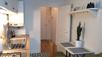 Een kleine keuken met een gasfornuis, spoelbak en een klok aan de muur.