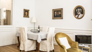 Un coin repas avec une table dressée pour deux personnes, une lampe et des portraits encadrés accrochés au mur.