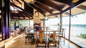 A spacious dining area with a stone fireplace, wooden chairs, and a view of a river.