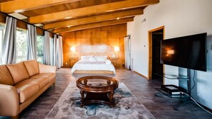 A spacious bedroom with a large bed, a wooden ceiling, a TV, and a leather sofa.