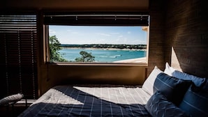 A bedroom with a large window overlooking a beach and ocean.
