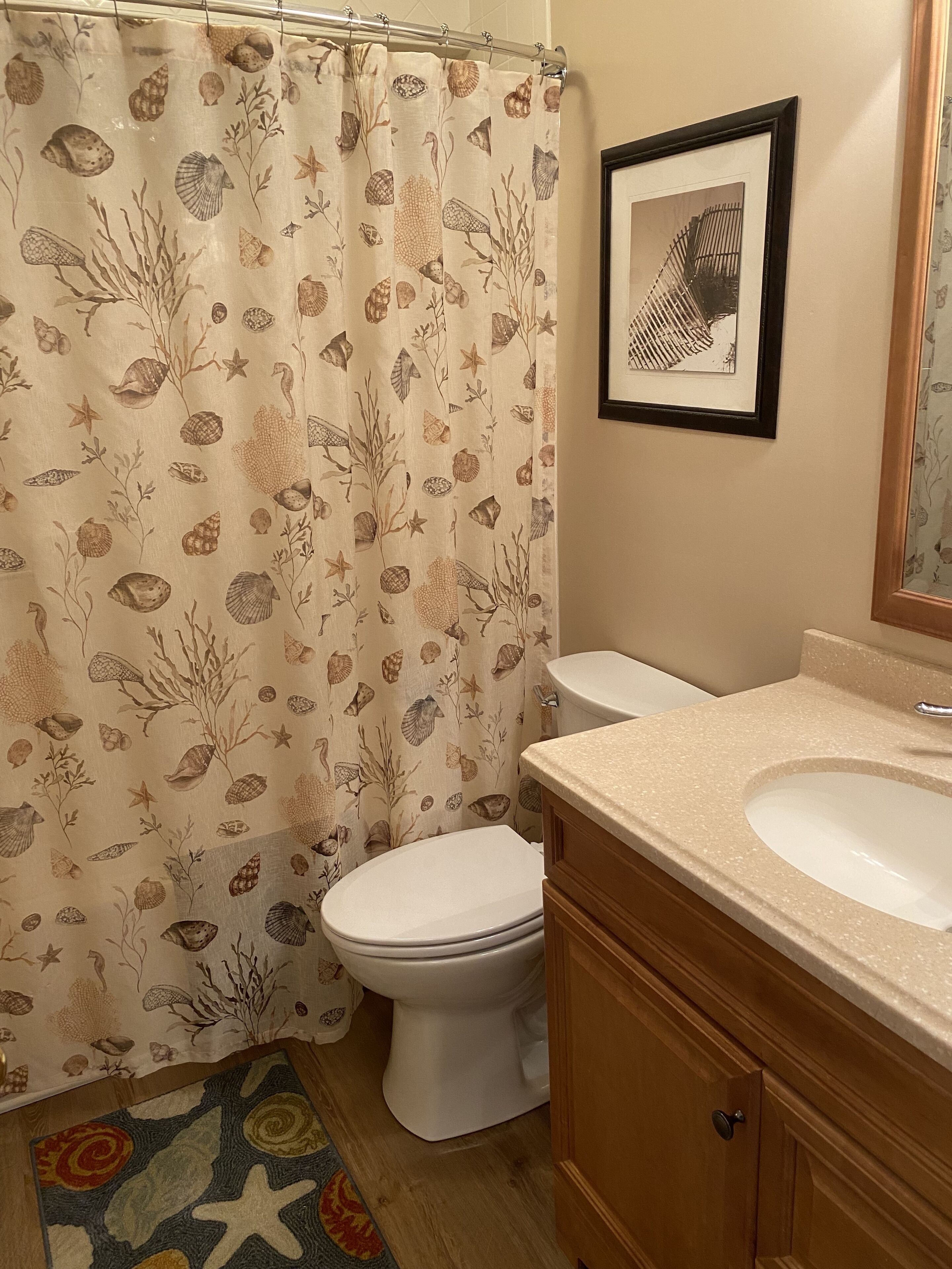 A bathroom with a shower curtain featuring a sea-themed pattern, a toilet, a sink with a countertop, and a framed picture on the wall.