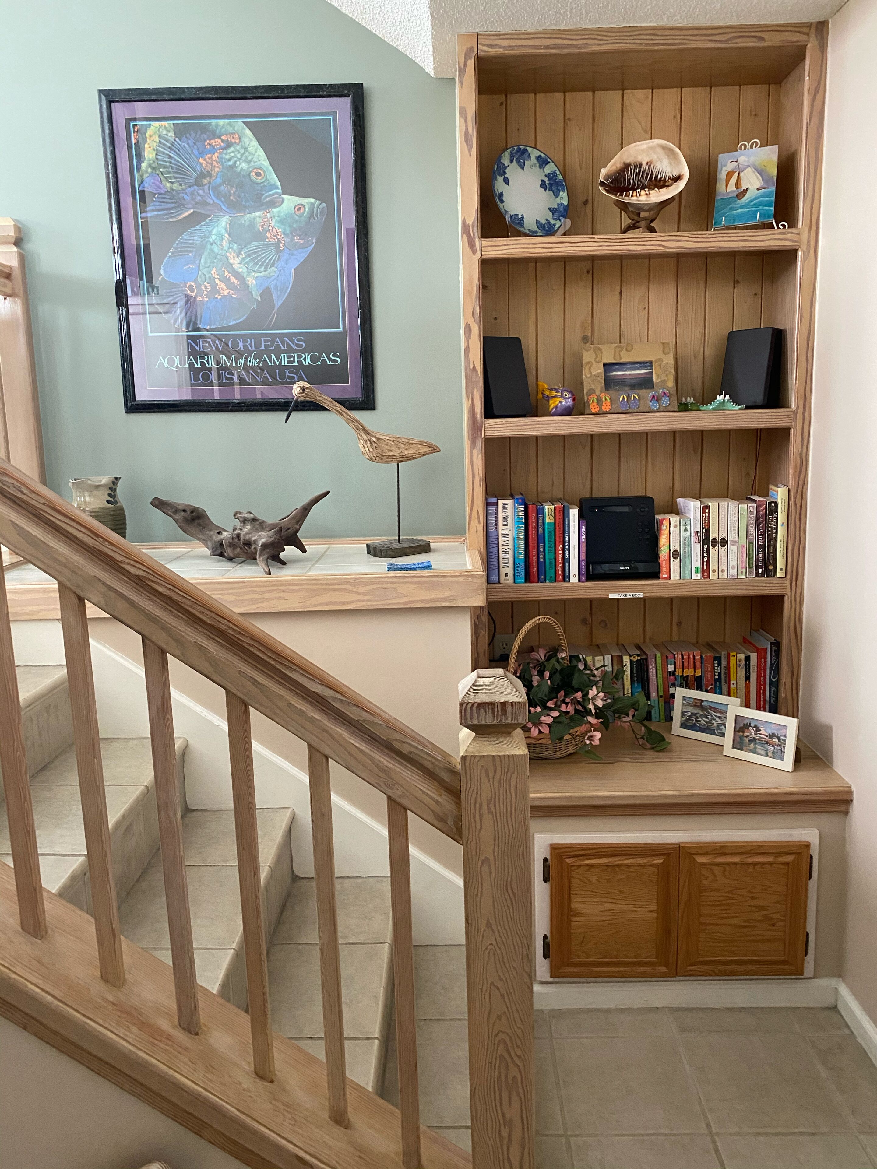 Eine Treppe mit Holzgeländern führt zu einer Empore mit einem Bücherregal, einem gerahmten Bild und einer kleinen Pflanze.