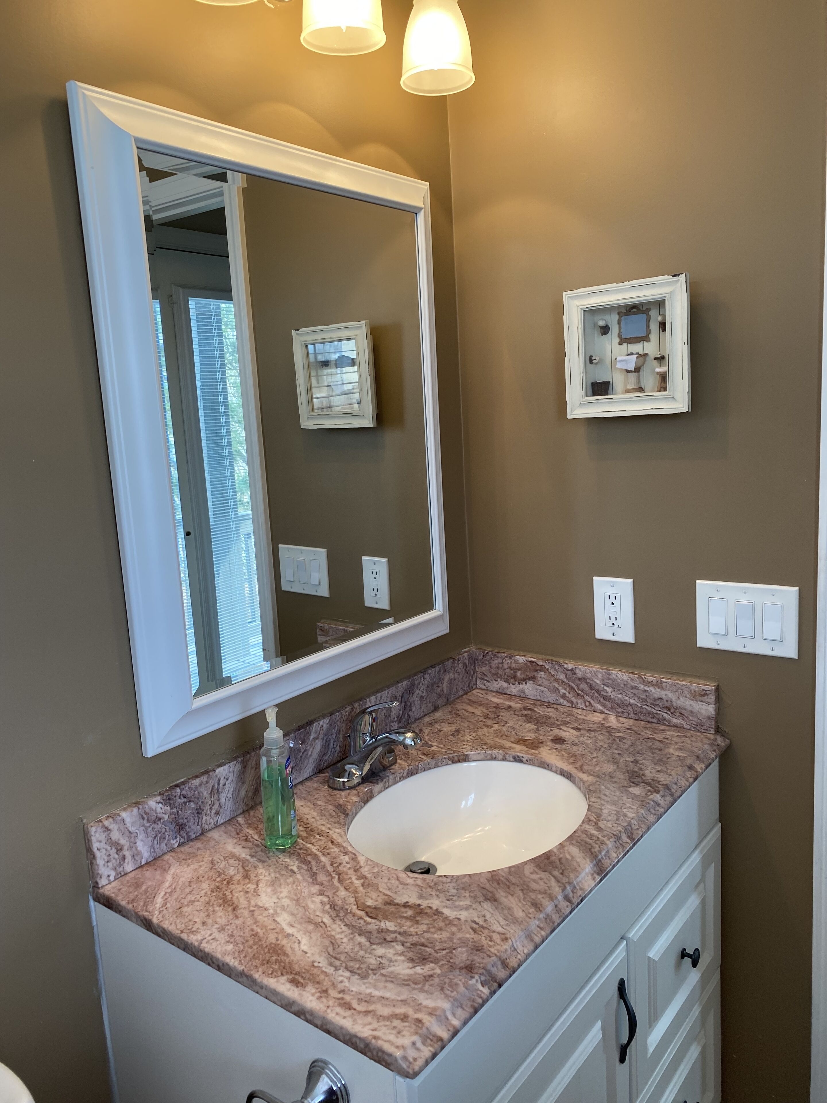 A bathroom with a white vanity, a sink, a mirror, and a wall-mounted light fixture.