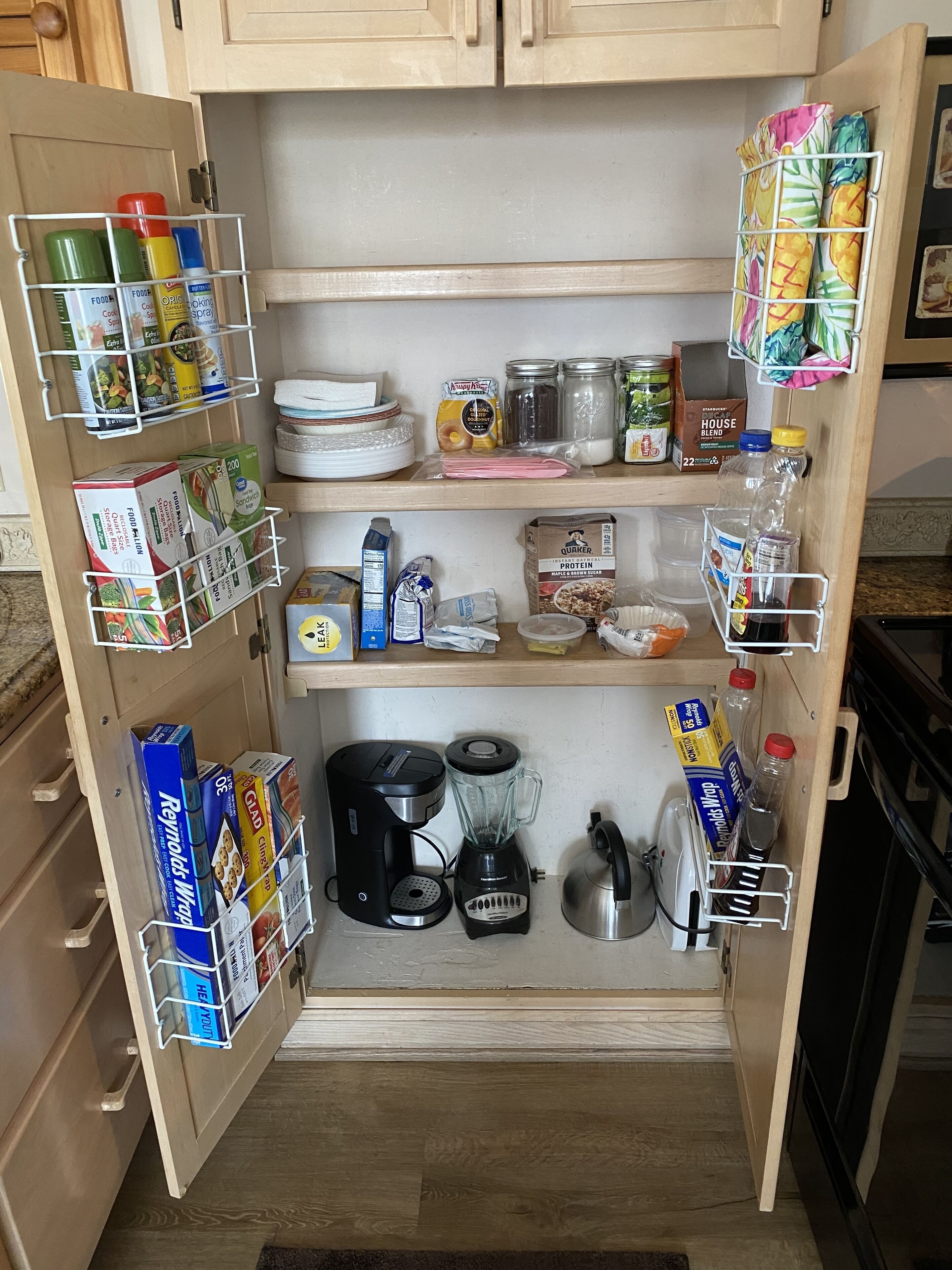 Una cocina con alacenas abiertas, estantes organizados y varios electrodomésticos.