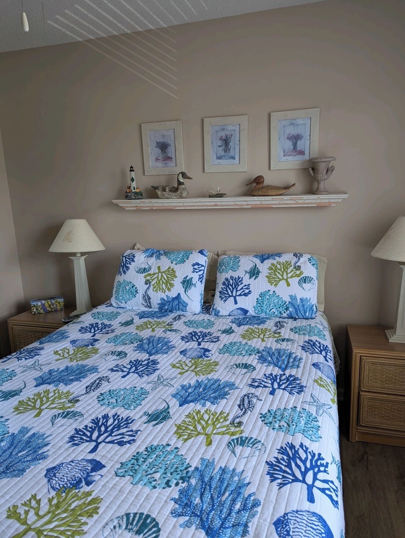 Un dormitorio con una cama, dos mesitas de noche, una estantería con adornos y cuadros en la pared.
