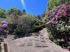 Un sentier de jardin bordé de dalles de pierre, entouré d’une végétation luxuriante et de fleurs aux couleurs vives.