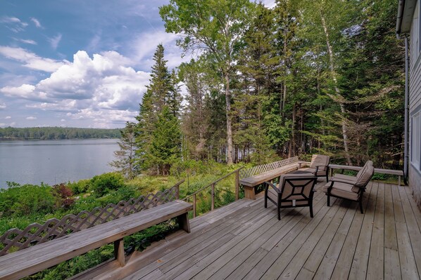 A wooden deck with outdoor furniture overlooking a lake, surrounded by trees.