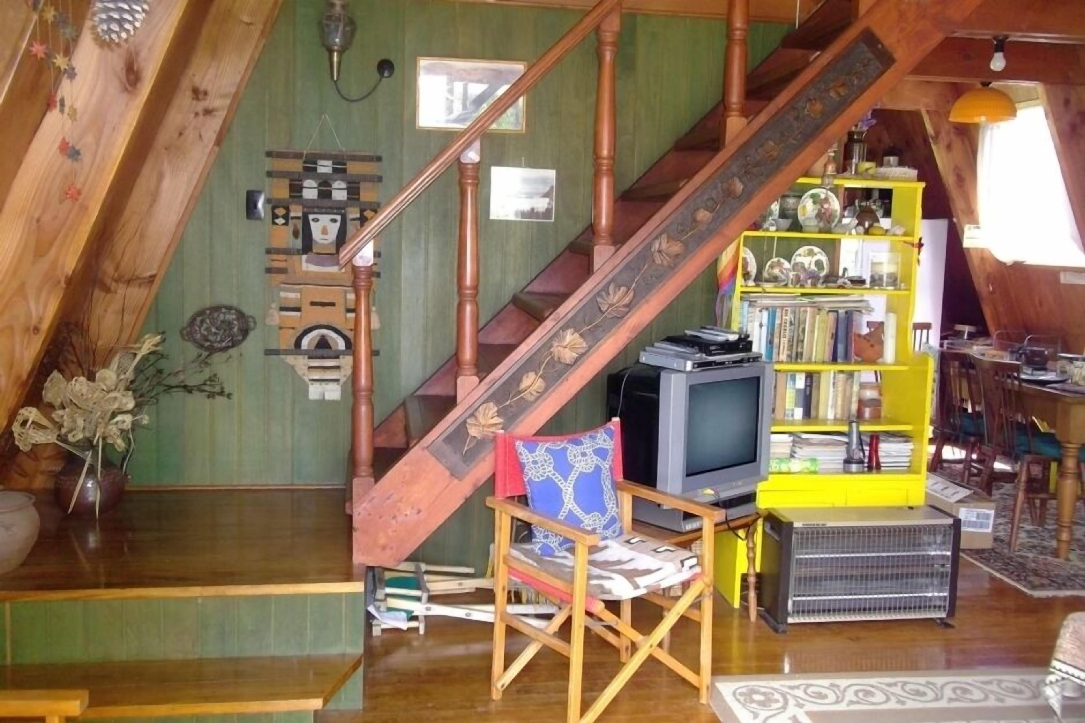 A loft-style room with a wooden staircase, a television, a bookshelf, and a chair.