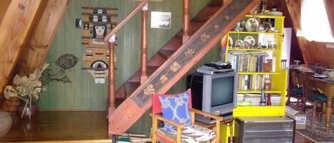 A loft-style room with a wooden staircase, a television, a bookshelf, and a chair.