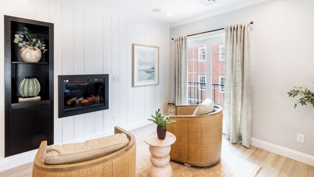 A living room with a fireplace, wicker furniture, a potted plant, and a view of a brick building through a window. - Condo w/Spiral Staircase to Loft, Perfect for Kids (Newport)