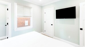 A room with a large window, a flat-screen TV mounted on the wall, and two white doors. - Condo w/Spiral Staircase to Loft, Perfect for Kids (Newport)