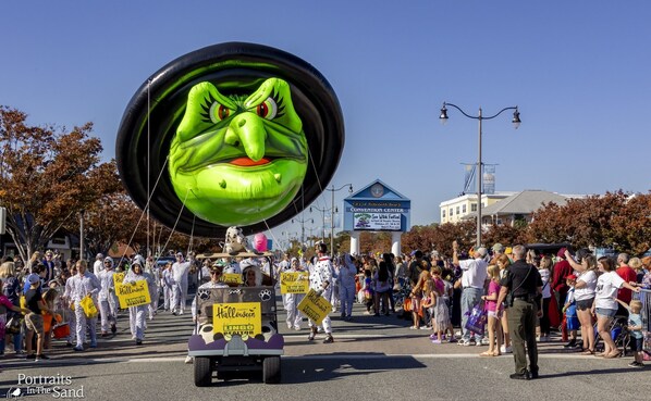 A parade with a large green inflatable character and a vehicle with Halloween-themed decorations.