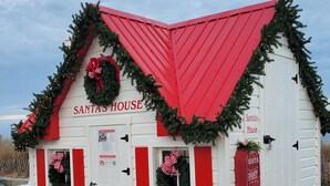 Een wit en rood Kersthuis versierd met kerstdecoraties, zoals kransen en guirlandes, met een bordje dat aangeeft dat het een te huur woning is.