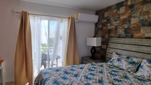 A hotel room with a bed, a nightstand, a lamp, a window with curtains, and a view of the outdoors. - Aventura Residences  (Lowlands)