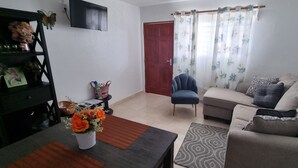 A living room with a sofa, a chair, a coffee table, a TV, and a door with curtains. - Aventura Residences  (Lowlands)