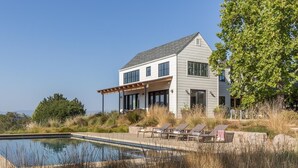 Une maison moderne à deux étages, dotée d’une piscine, d’un espace extérieur aménagé et offrant une vue sur le paysage.