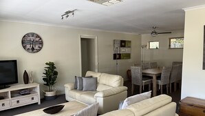 Ett vardagsrum med en beige soffa, en tv, ett matbord med stolar och en takfläkt.