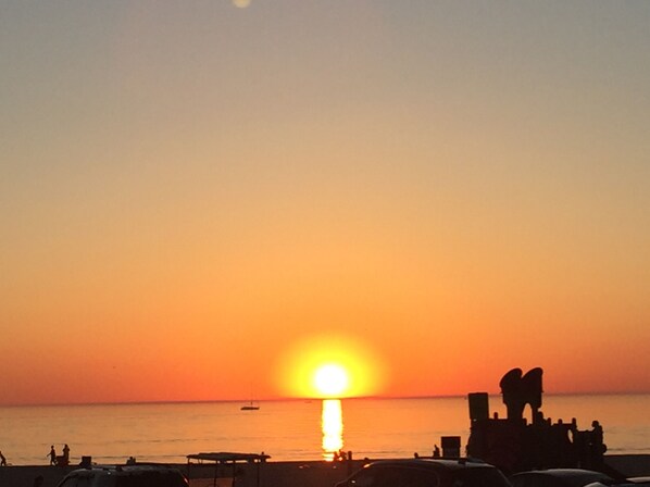 A sunset over a beach with silhouettes of people and a boat.