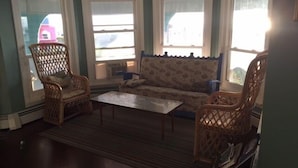 Ein Wohnzimmer mit einer Couch, zwei Korbsesseln, einem Couchtisch und großen Fenstern.